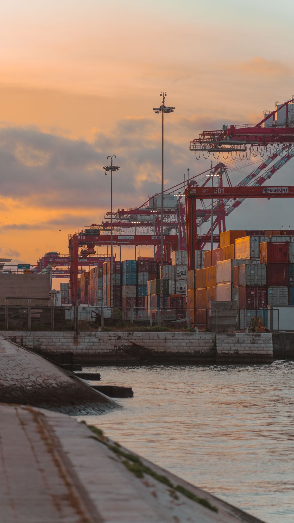 Cargo containers and port cranes beside the water at sunset.